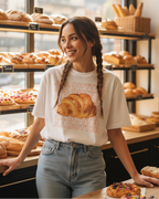 White t-shirt with a croissant graphic and 'All Butter' text on a model in a bakery.