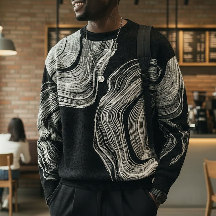 Person wearing a black sweater with white abstract patterns, standing against a neutral background.