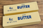 2 sticks of Butter Me Up Squishy - 4 oz butter on a wooden farmhouse table.