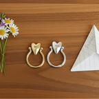 Two heart-shaped rings, one gold and one silver on a wood surface.