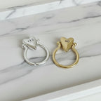 Two heart-shaped rings, one silver and one gold, on a marble surface.