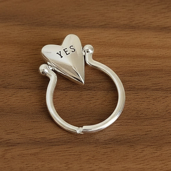 Silver ring with 'YES' on a walnut wood surface.