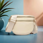 Cream Baye Bag with gold accents on a blue surface with a plant in the background