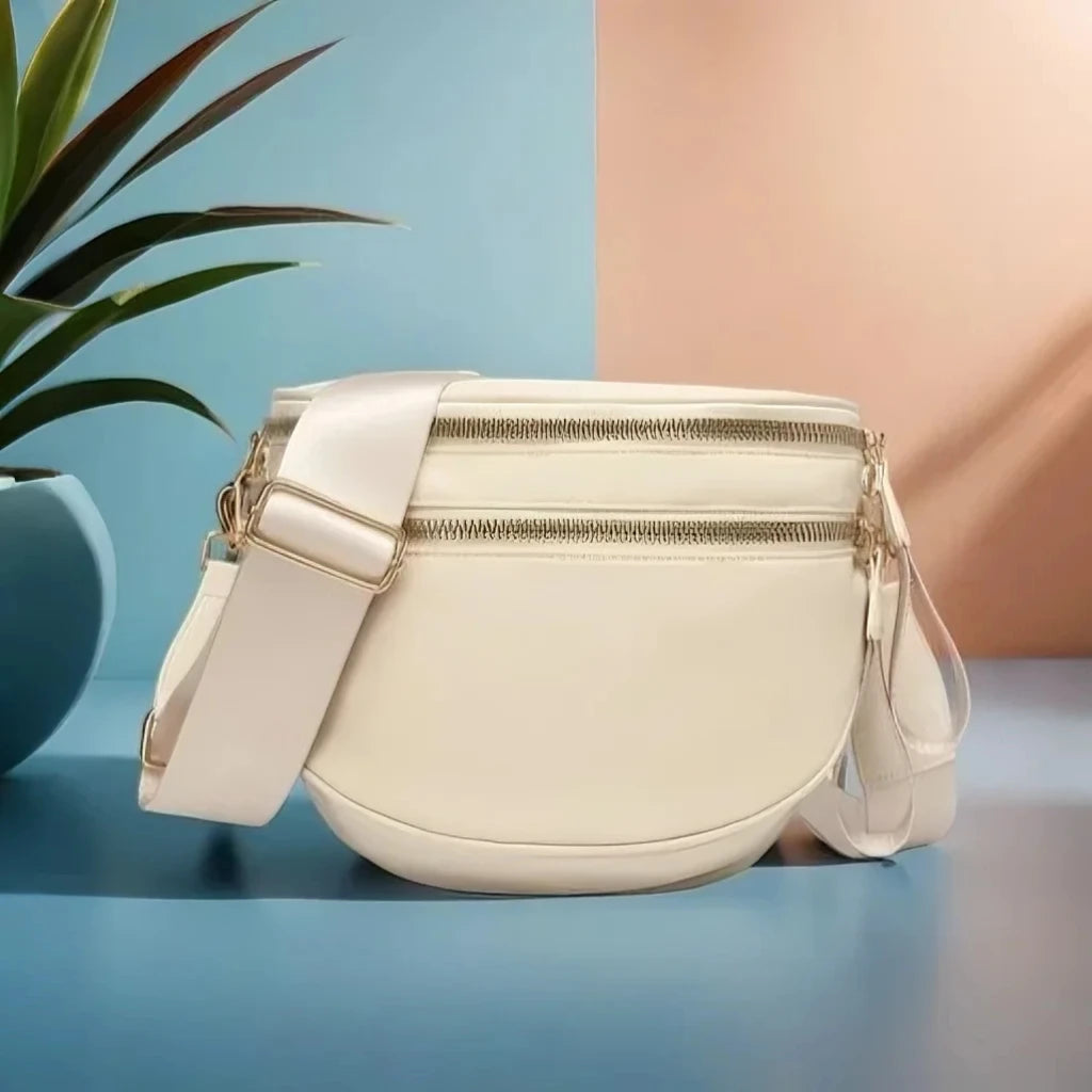 Cream Baye Bag with gold accents on a blue surface with a plant in the background