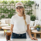 Woman on a patio wearing a 'Diet Coke' cap and holding a glass of iced soda.