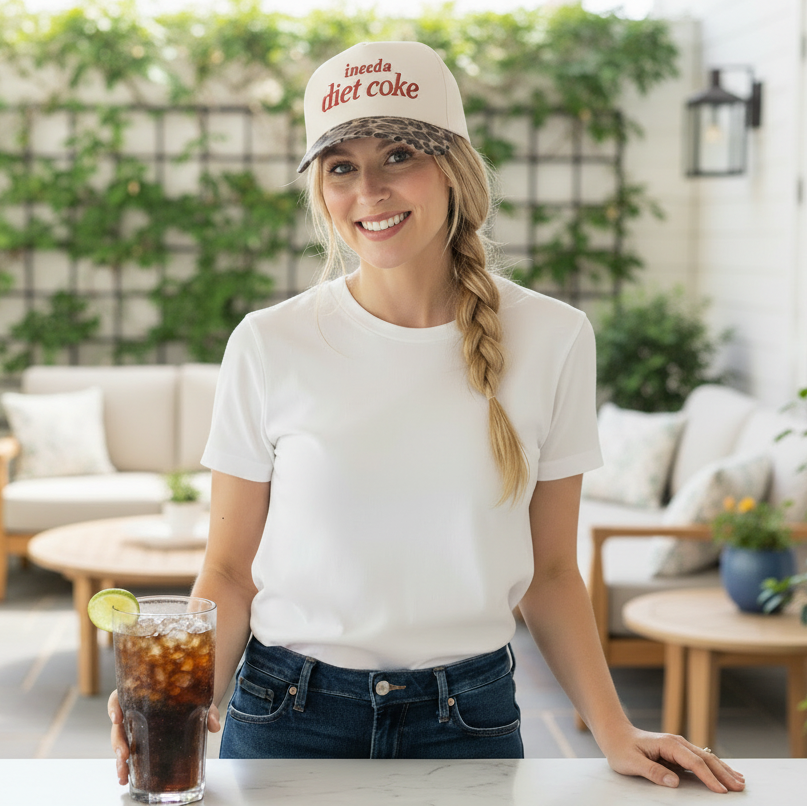 Woman on a patio wearing a 'Diet Coke' cap and holding a glass of iced soda.