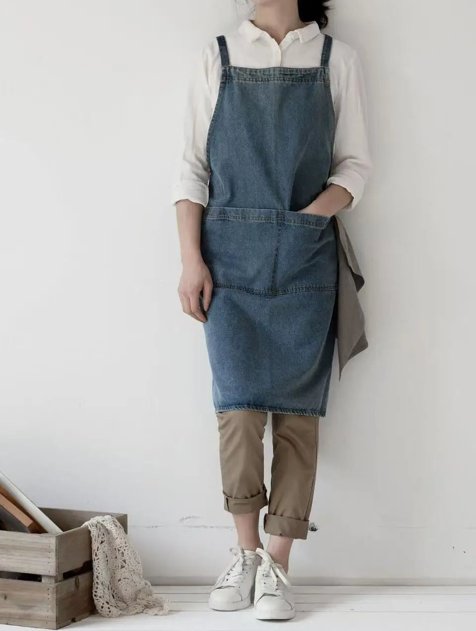 Person wearing a denim apron over a white shirt with a plain background