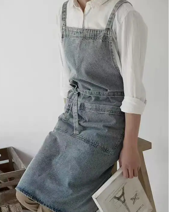 Person wearing the Draper Denim Apron holding a book in a minimalistic setting