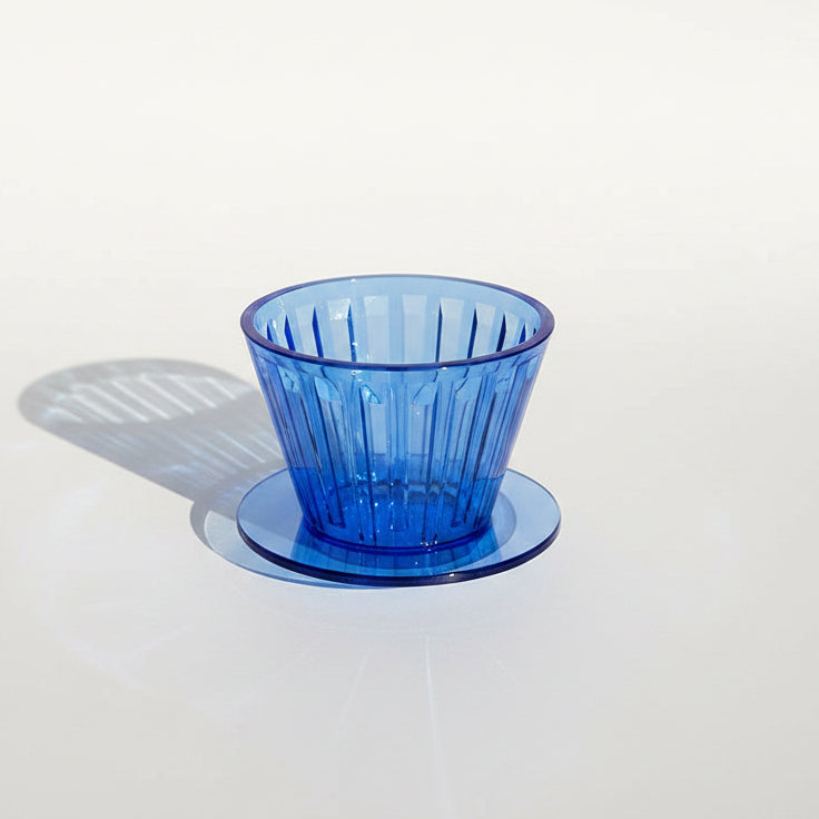 A translucent cobalt blue plastic cup with a vertical ribbed texture, sitting on white surface under direct sunlight.
