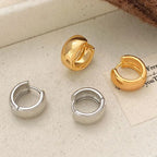 Four small hoop earrings arranged on a light beige fabric surface: two silver-toned hoops and two gold-toned hoops, with one gold hoop standing upright.