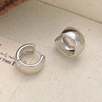 A pair of polished silver huggie hoop earrings resting on a textured beige fabric surface.