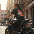 Woman sitting on a motorcycle wearing a black t-shirt with a Keep It Twisted graphic in an urban setting.