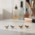 Mini croissant silver & gold earrings on a marble surface with blurred makeup items in the background. 