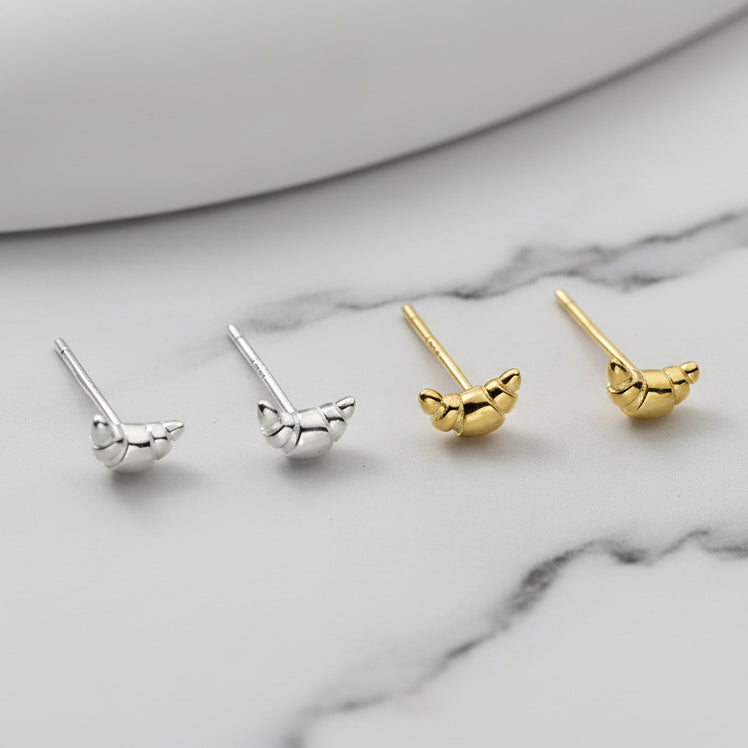 Two pairs of mini croissant-shaped earrings, one silver and one gold, on a marble background.