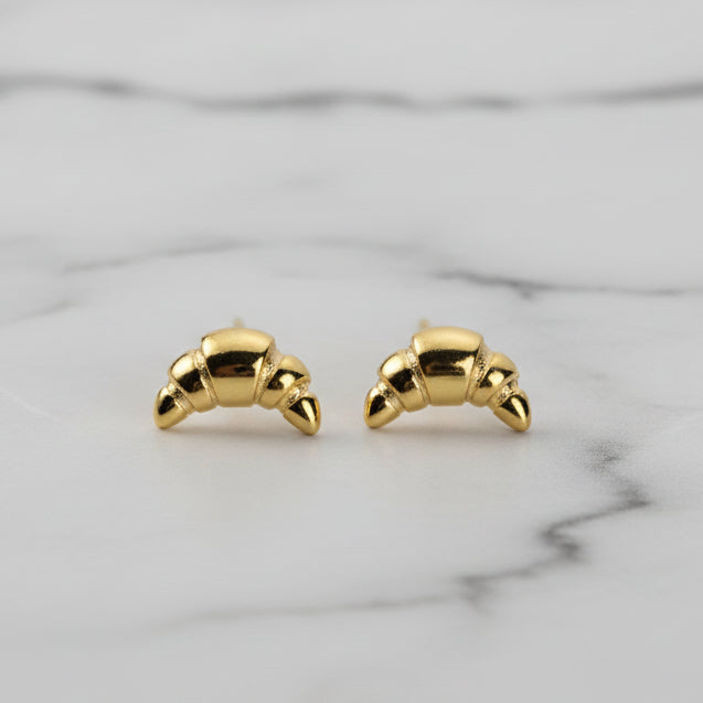 Gold croissant earrings on a marble surface.