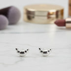 Silver mini croissant-shaped earrings on a marble surface with makeup in the background.