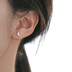 Close-up of a model's ear wearing a silver mini croissant-shaped earring on a neutral background.