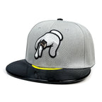 A gray snapback cap featuring a black brim, a yellow accent line under the brim, and a white embroidered hand graphic with a brown box on the front.