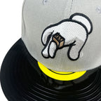 Close-up of a gray snapback cap featuring an embroidered cartoon hand holding a brown box labeled 'GTS', with a bright yellow visor band and black brim.