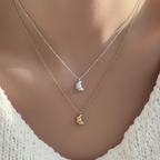 Two necklaces with croissant pendants on a mannequin wearing a white top.