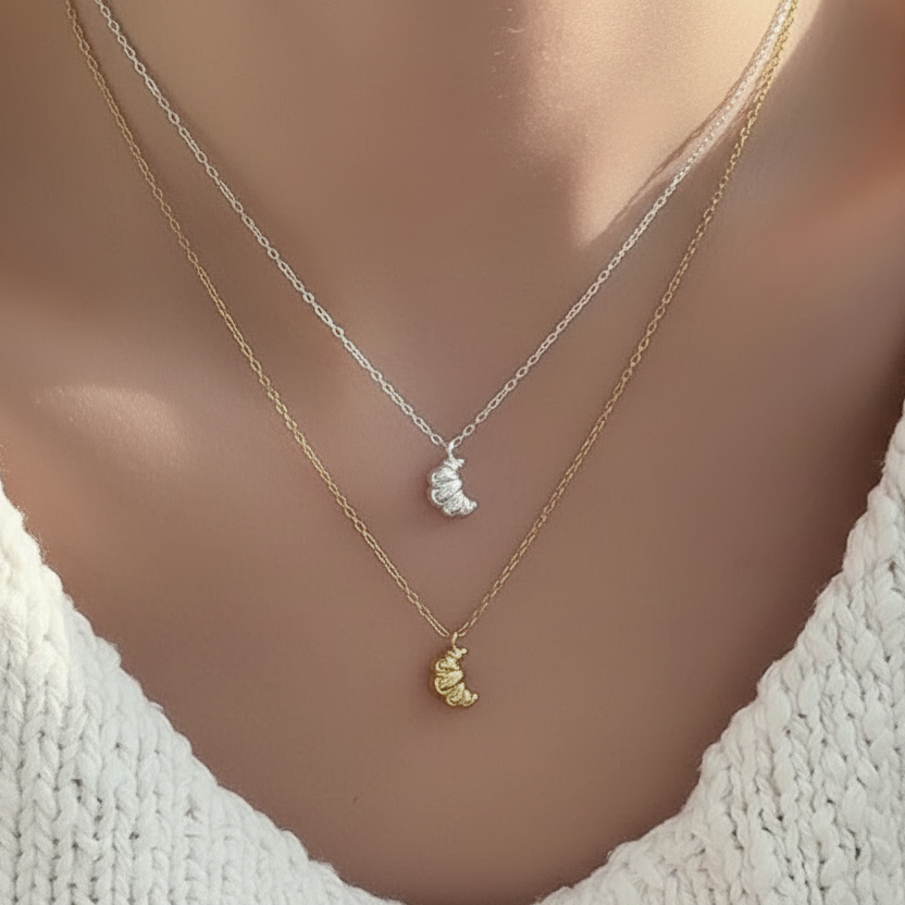 Two necklaces with croissant pendants on a mannequin wearing a white top.