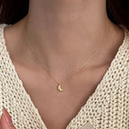 Necklace with a croissant pendant worn by a person in a beige sweater.