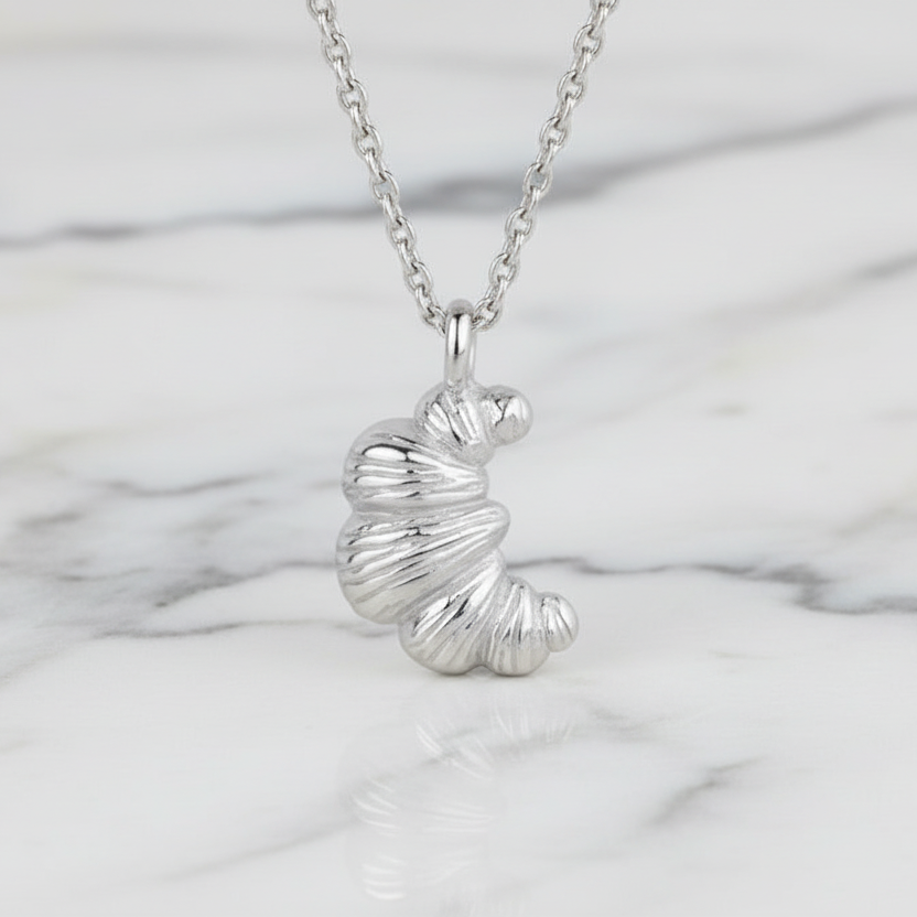 Silver croissant necklace with a unique pendant on a marble surface