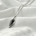 Silver necklace with a shield-shaped pendant on a textured white surface