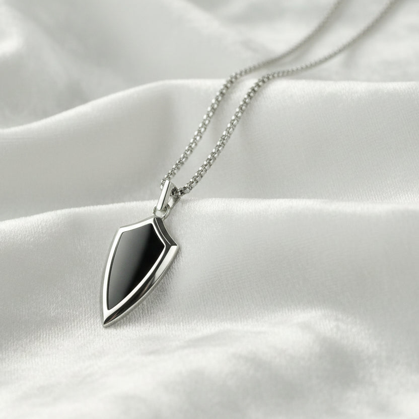 Silver necklace with a shield-shaped pendant on a textured white surface