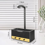 A tabletop speaker-shaped headphone stand with a black body, yellow front panel, and curved black headphone arm, shown with dimension labels over a white interior background with blinds and a vase.