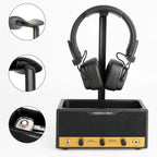 Black headphone stand holding a pair of black over-ear headphones, shown with three circular detail insets highlighting the earcup, stand arm, and interior charging tray. The stand has a gold front panel with control knobs and the text 'headphone stand'.